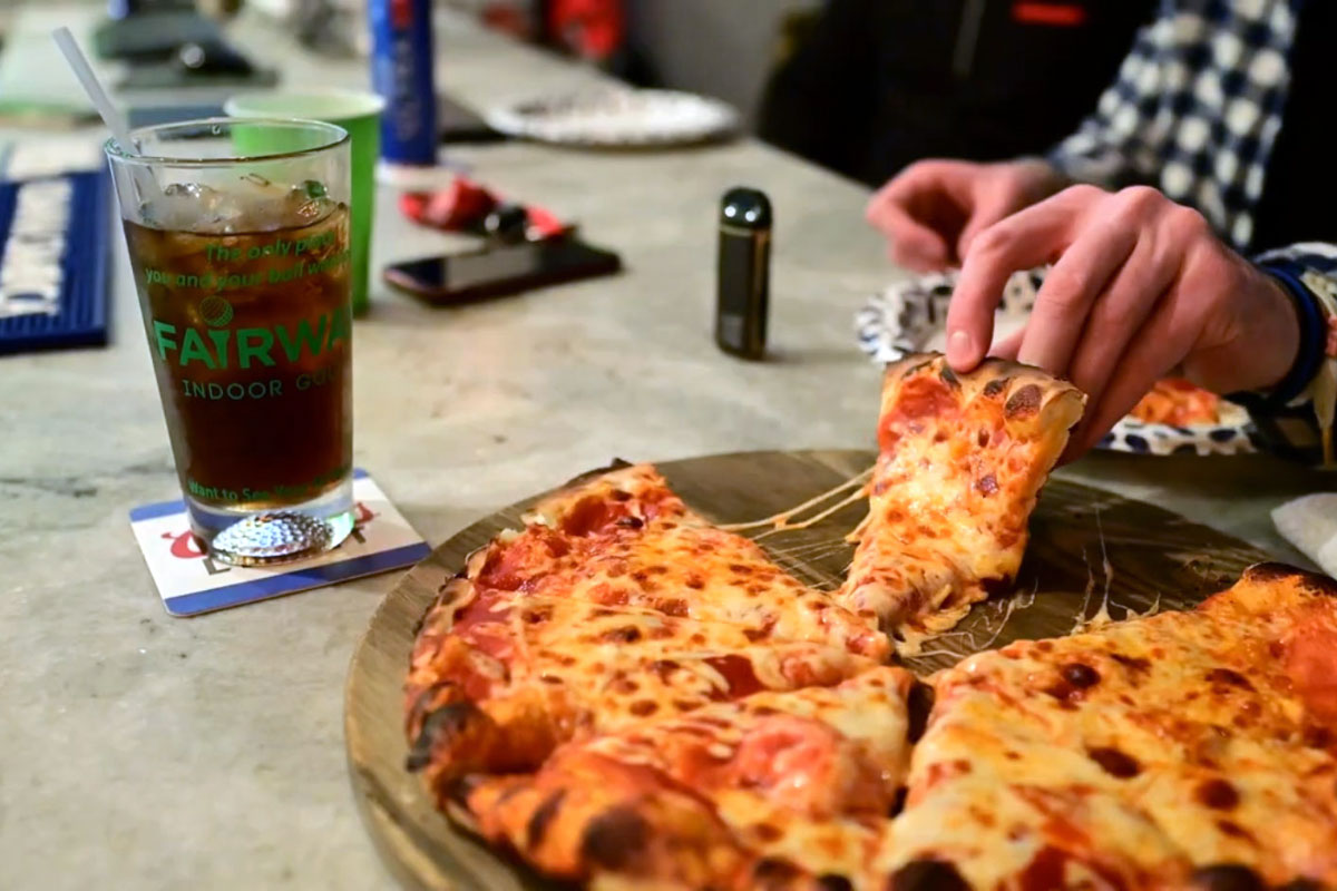 Hand pulls slice of pizza from wooden serving board